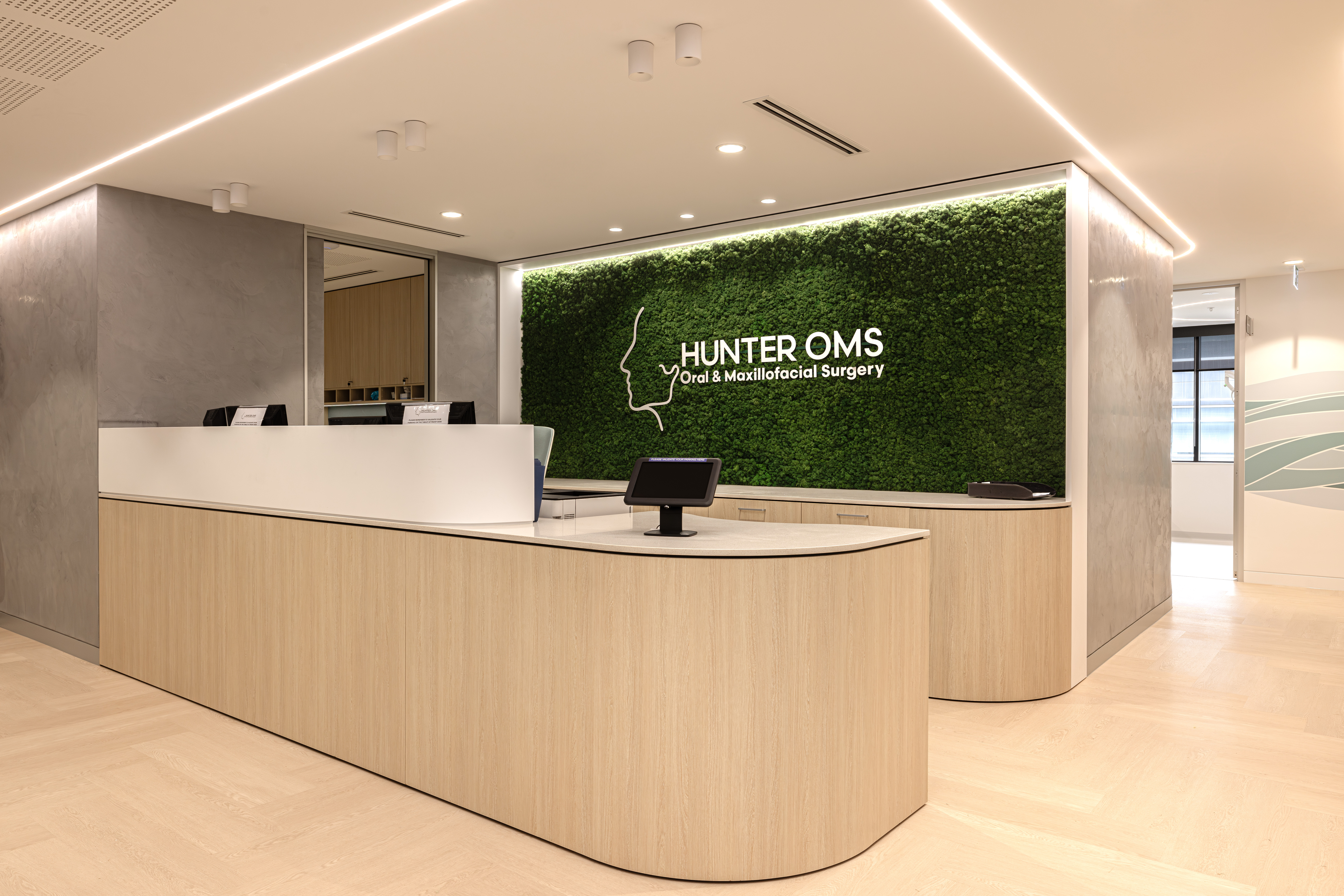 Medical reception fitout with a curved timber desk and green Hunter OMS feature wall.