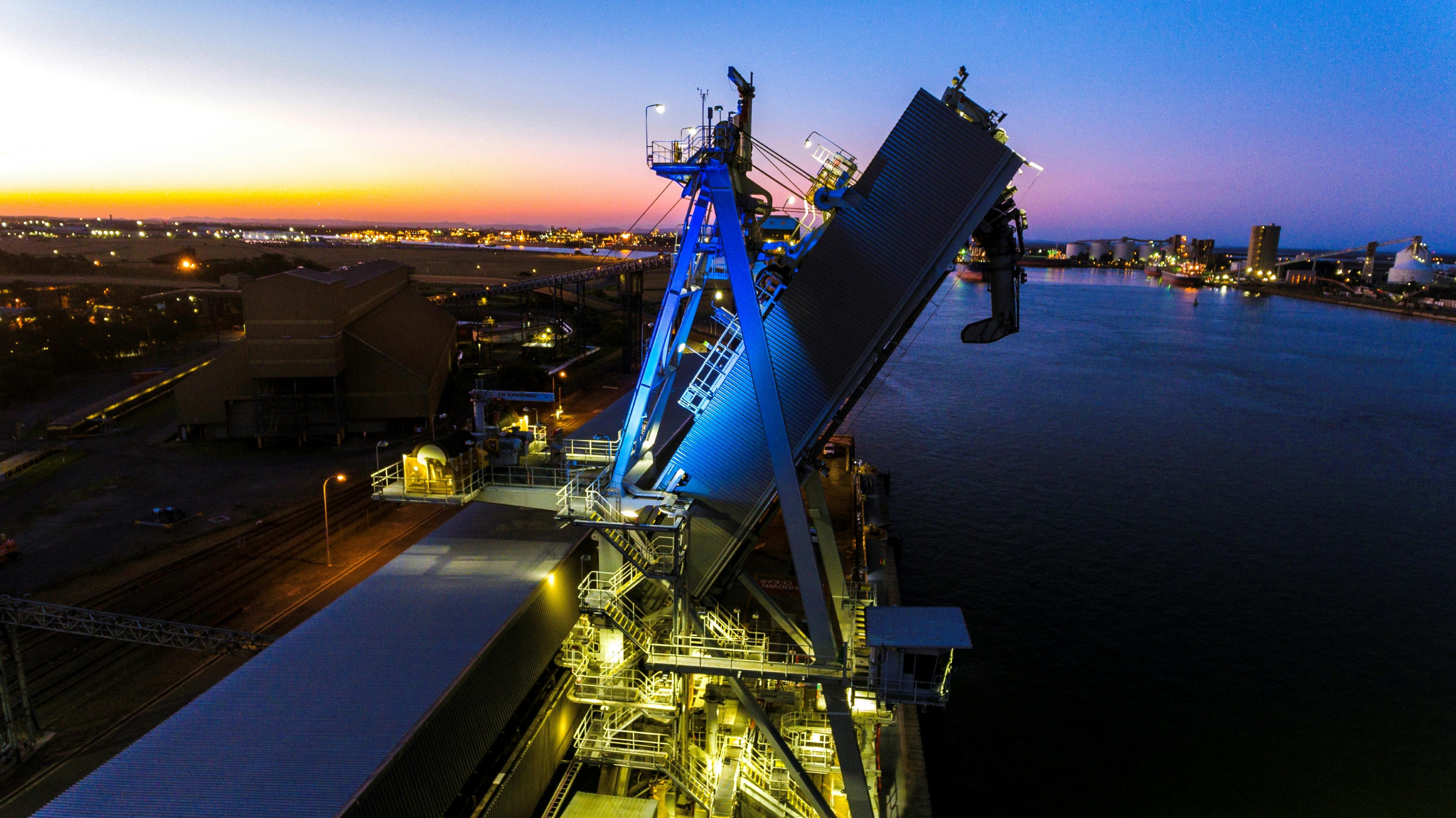 Port Waratah shiploader illuminated blue beside Newcastle Harbour at dusk.