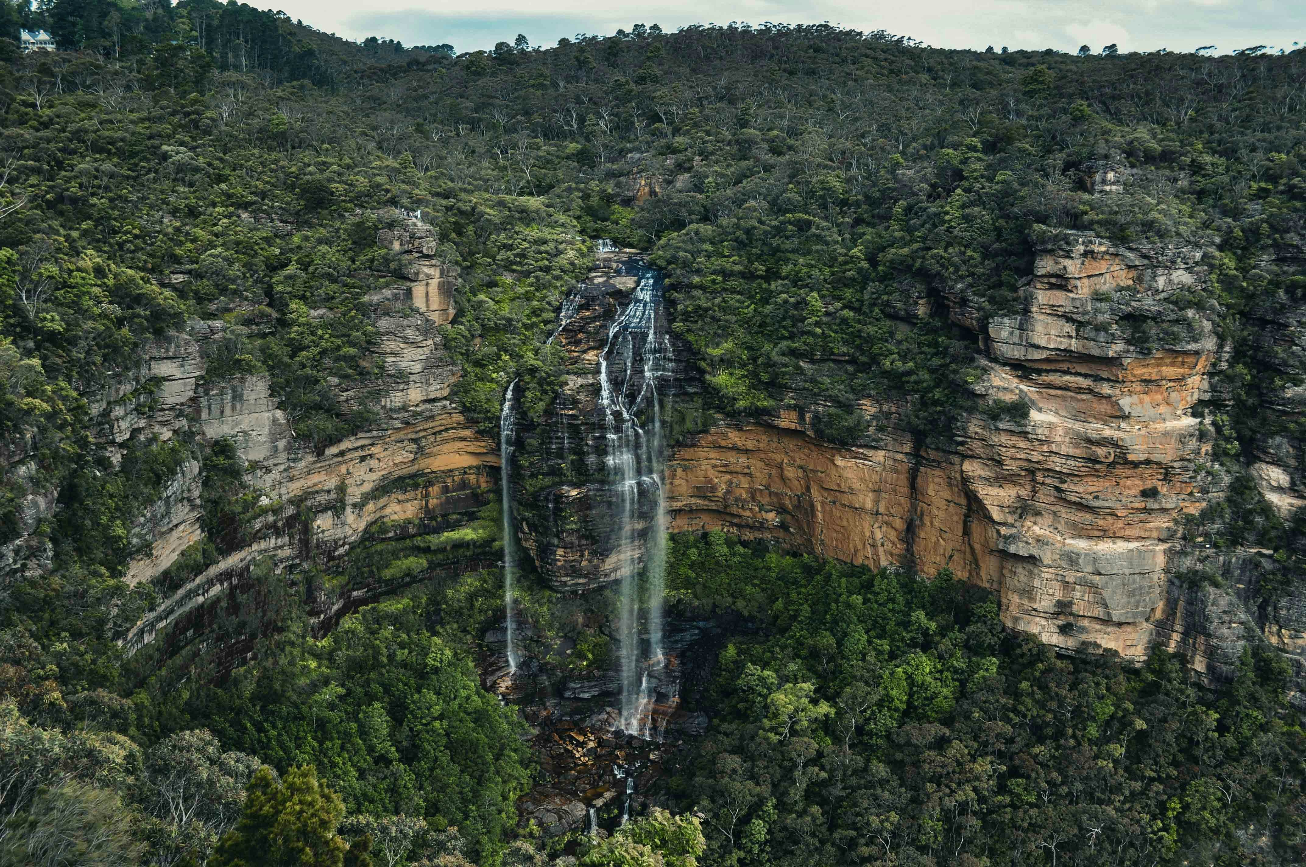 Waterfall flowing through forested sandstone cliffs.