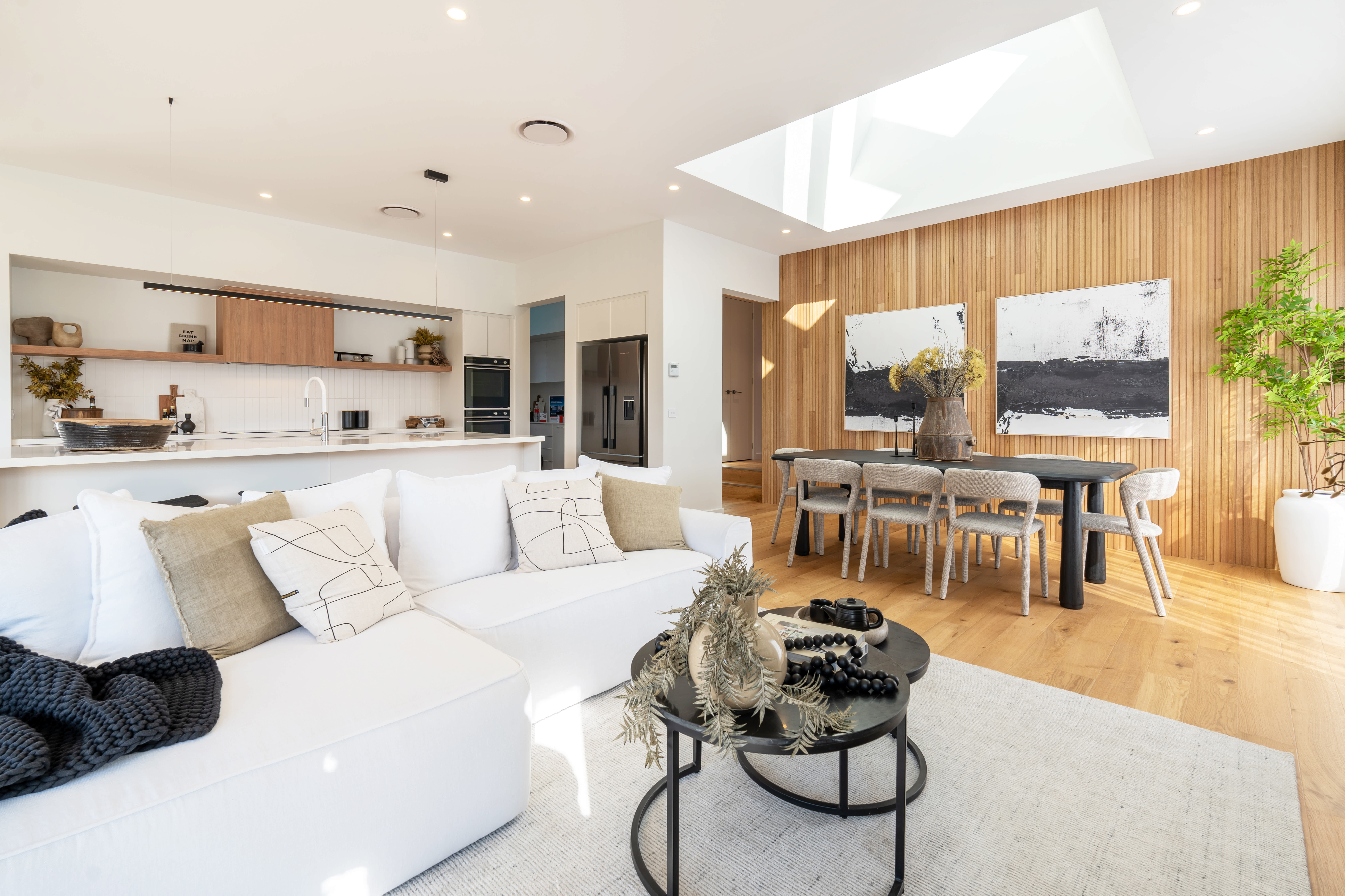Wilson Homes interior with a white sofa, timber dining wall and open-plan kitchen.