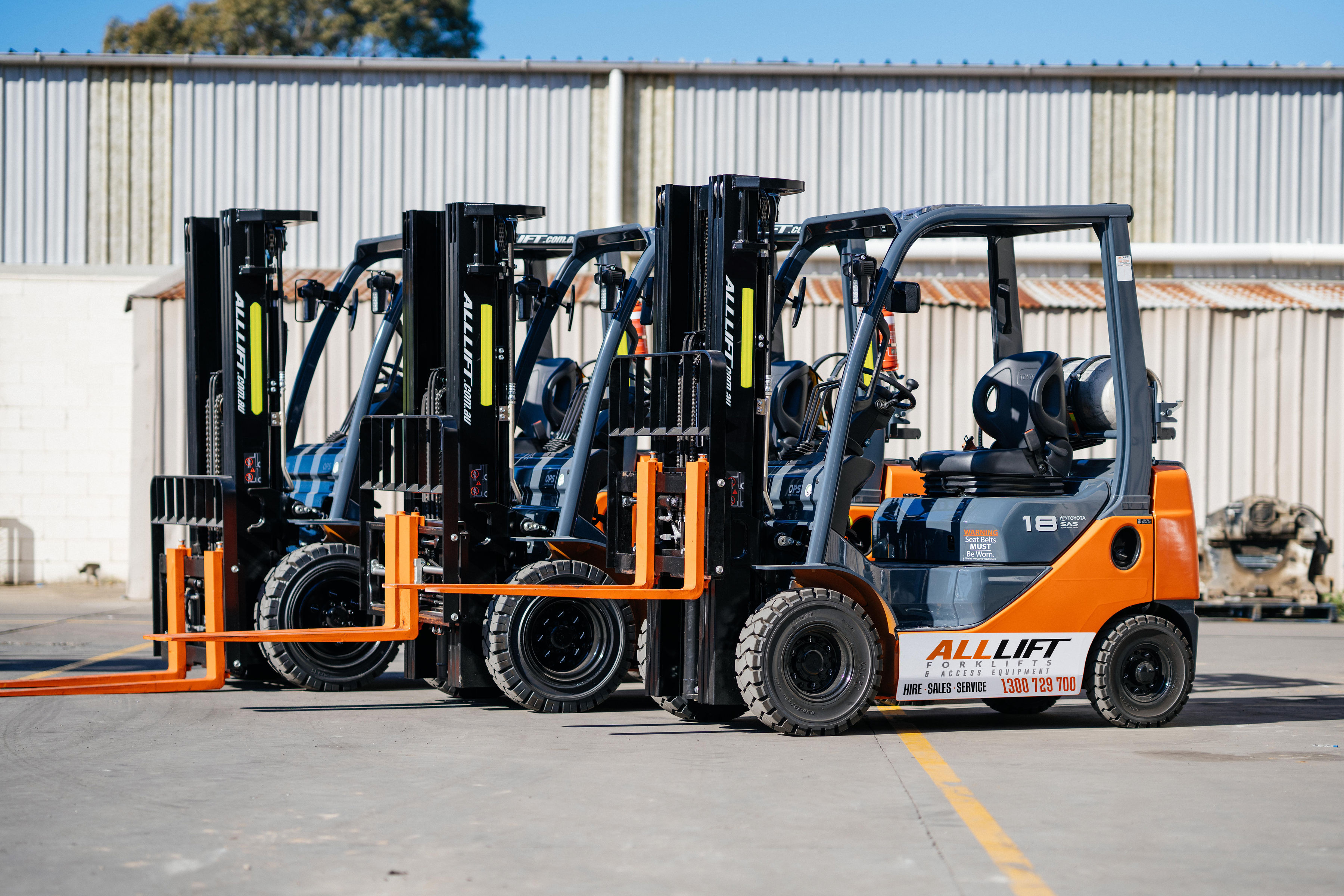 All Lift branded Toyota forklifts lined up outside a workshop.